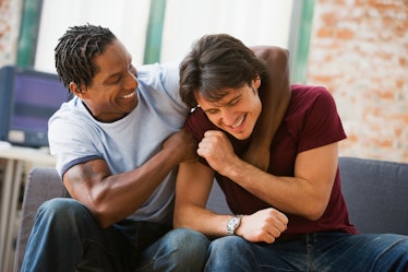 A man has another man in a headlock as they sit on a couch, laughing.