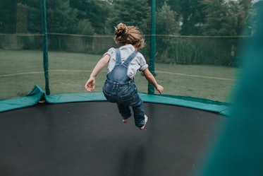A child in overalls jumps on a trampoline.