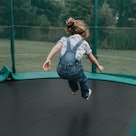 A child in overalls jumps on a trampoline.