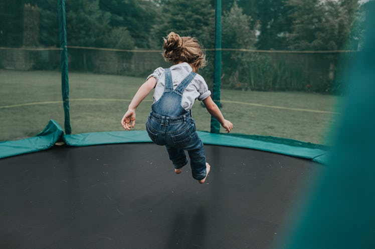 A child in overalls jumps on a trampoline.