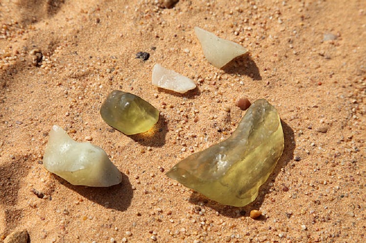 photo of 5 chunks of yellow glass sitting on sand