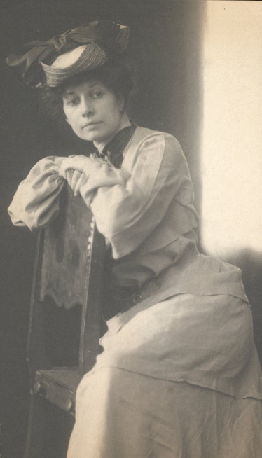 A black-and-white portrait of a woman in a hat sitting on a chair