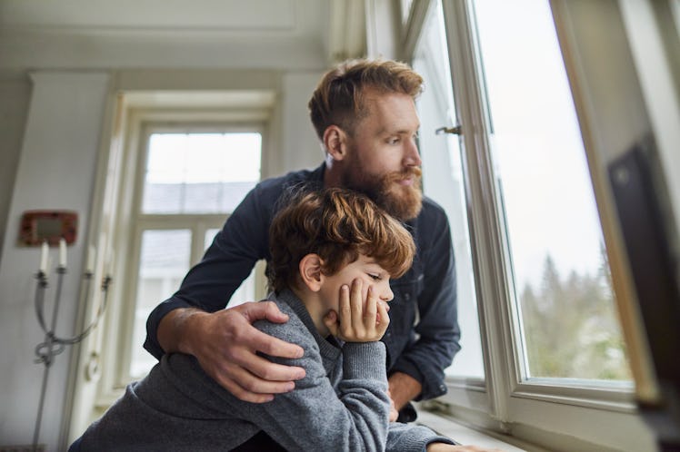 A worried dad and child looking out a window at home.