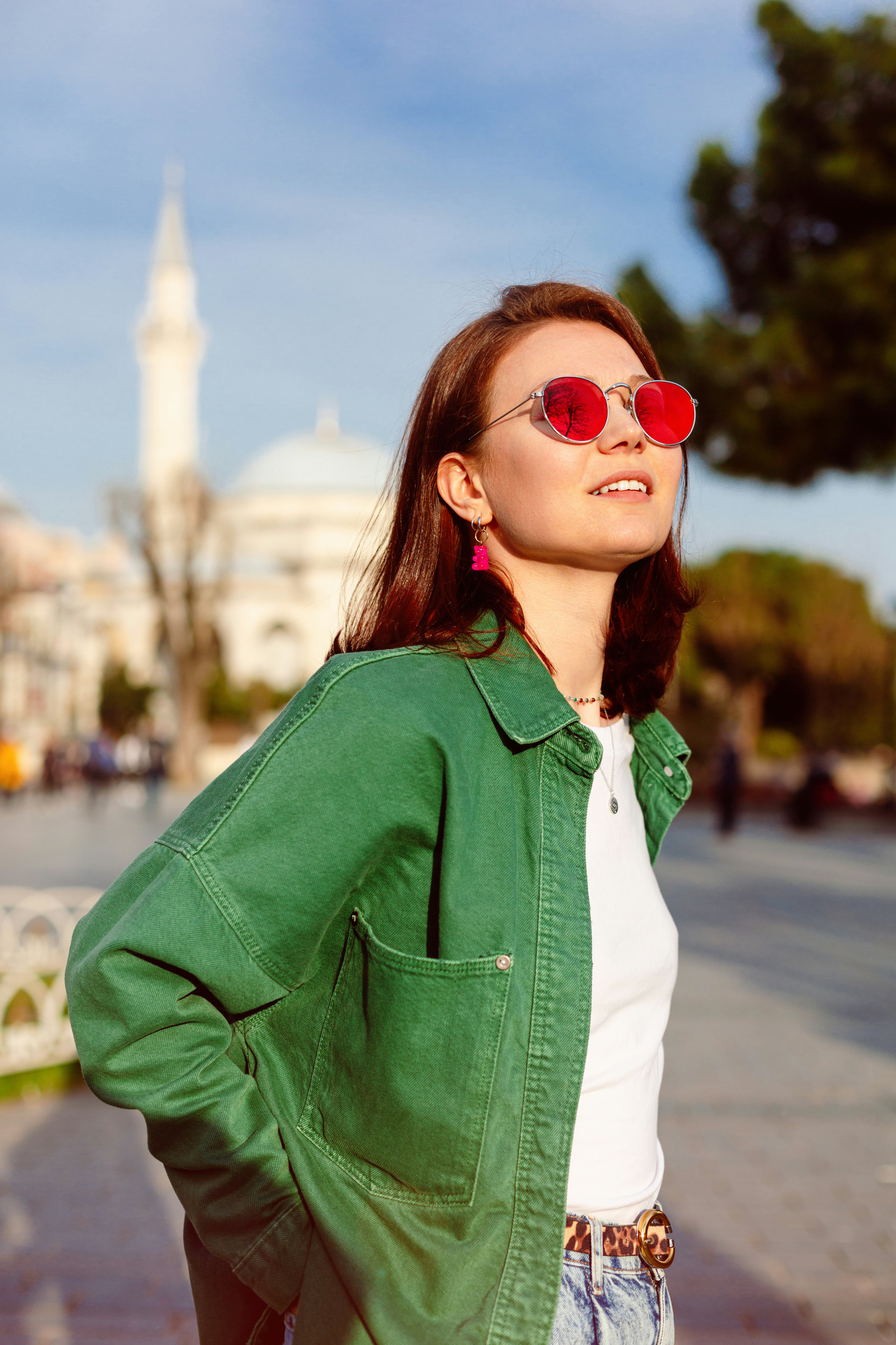 Young woman wearing red sunglasses and smiling in the street, thinking about her zodiac sign's lucky...