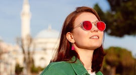 Young woman wearing red sunglasses and smiling in the street, thinking about her zodiac sign's lucky...