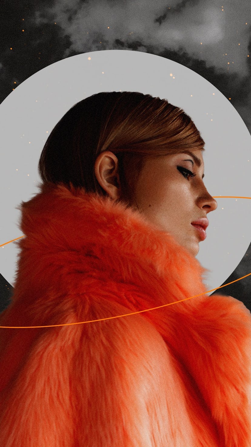 Young woman wearing a furry, orange coat in front of the moon during Uranus retrograde 2022.