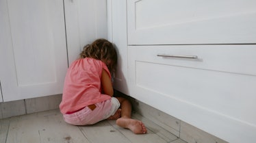A girl getting a timeout in a corner of a room, facing away.