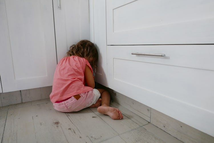 A girl getting a timeout in a corner of a room, facing away.