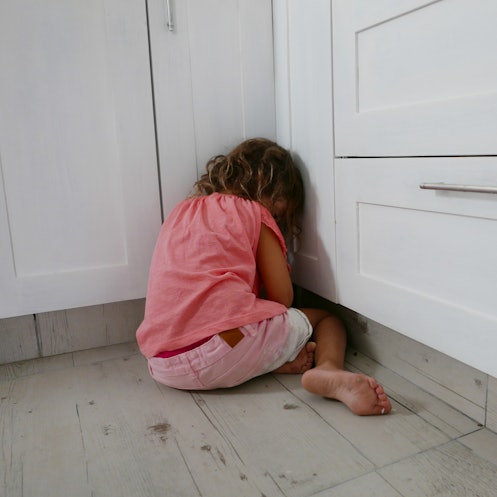 A girl getting a timeout in a corner of a room, facing away.