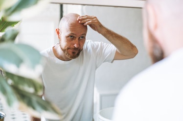 A balding man checks his head in a mirror for hair loss.