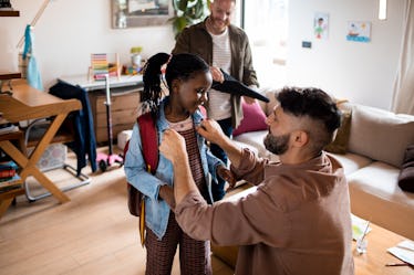 Two dads help their daughter get ready for school at home in the morning.