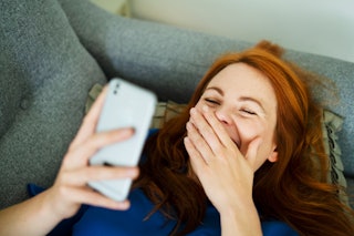 A woman giggles while reading a phone. 