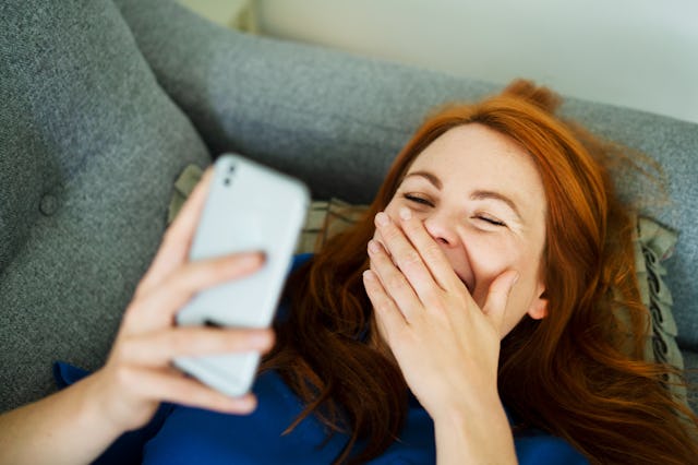 A woman giggles while reading a phone.