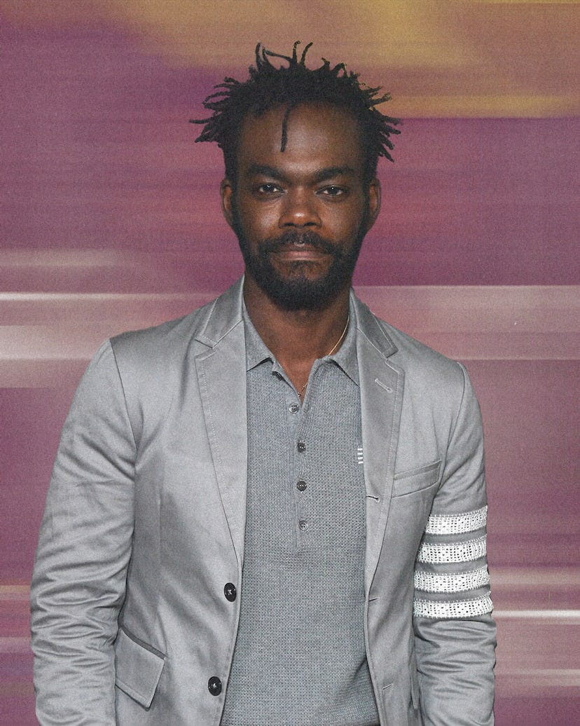 A portrait of William Jackson Harper in a grey shirt and a grey blazer with a blurred pink backgroun...
