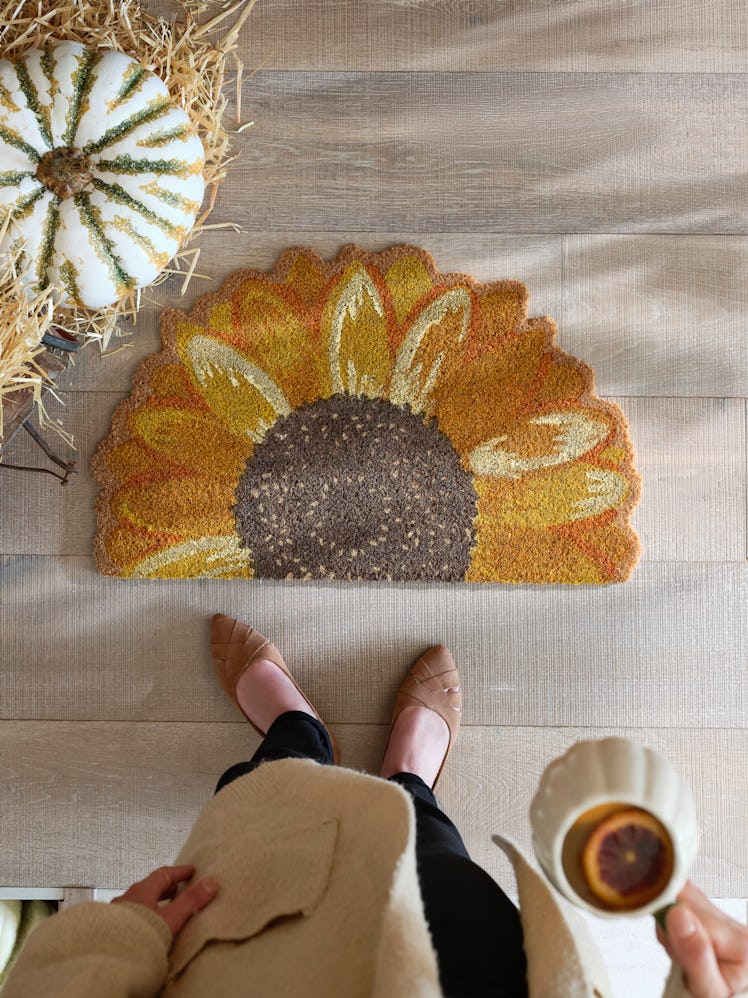 A woman stands with a sunflower doormat, which is one of the fall 2022 home decor trends, according ...