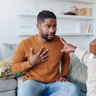 Woman pointing at man as they sit on couch having argument