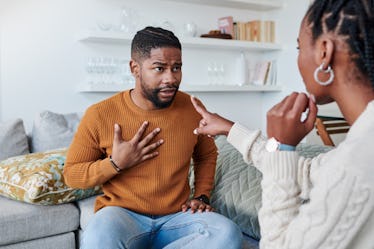 Woman pointing at man as they sit on couch having argument