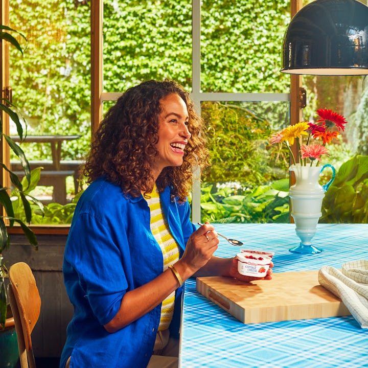 Curly-haired woman sitting at kitchen table eating cottage cheese with strawberry jam