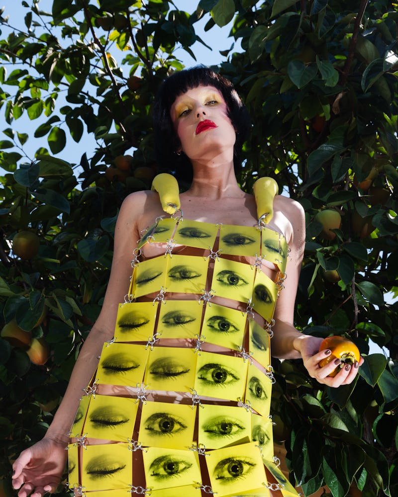 A black-haired woman posing in a yellow dress with black eyes