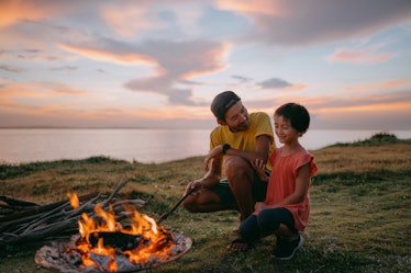 A dad and his daughter build a fire on the beach.
