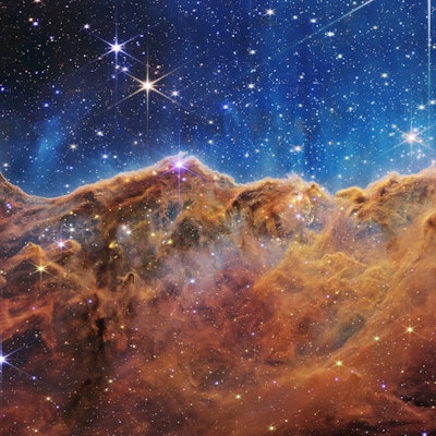 Dusty, dark mountainous regions contrast a blue background with thousands of stars visible all over ...