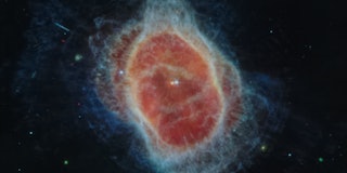 Contrasting colors create an oval-shaped, dusty nebula dotted with small stars against a black backg...