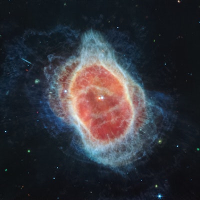 Contrasting colors create an oval-shaped, dusty nebula dotted with small stars against a black backg...