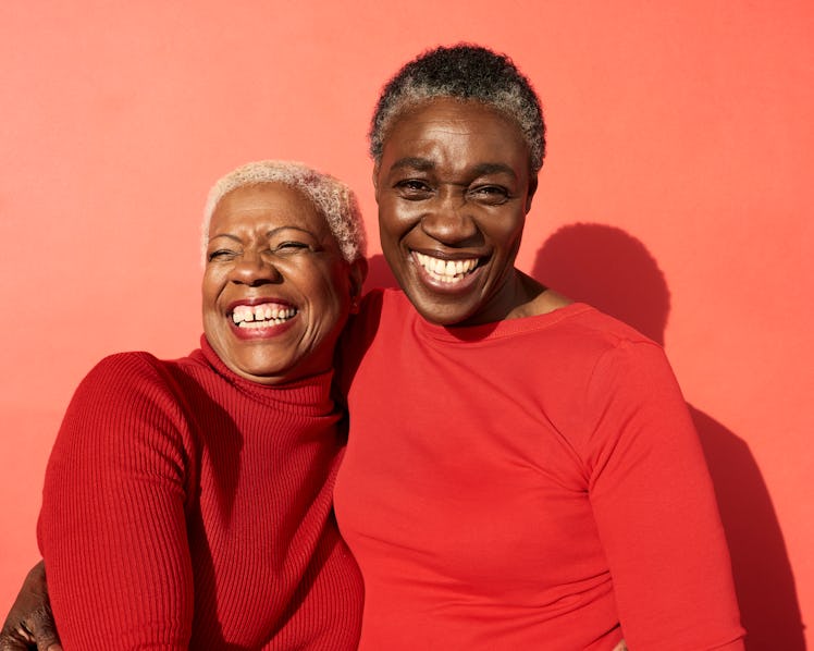 Two female friends dressed in red hugging and smiling.