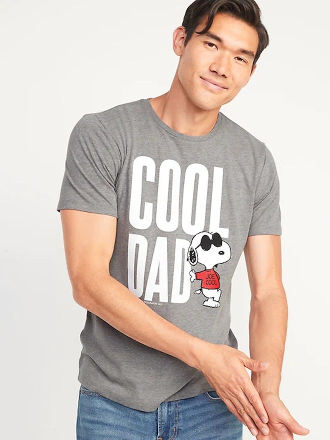 A man wearing a grey t-shirt with snoopy in sunglasses on it and text that says cool dad in an artic...