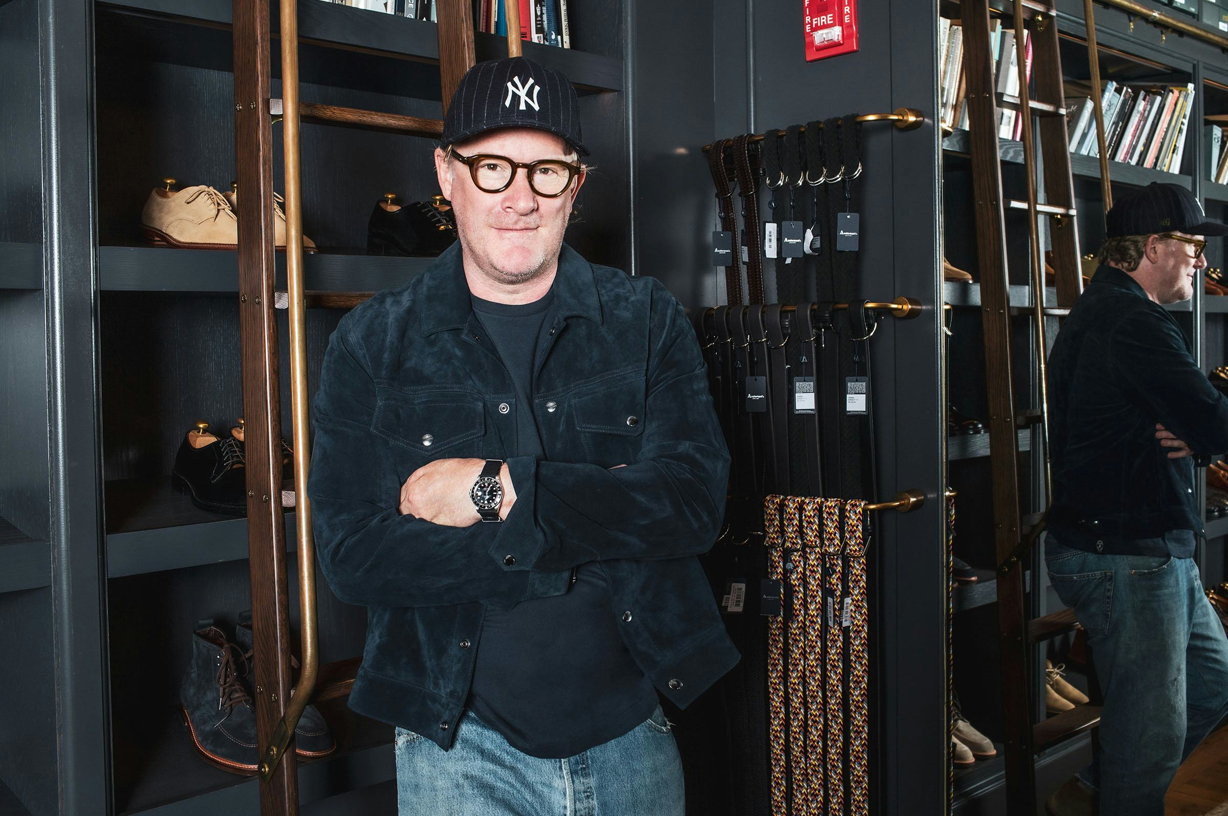 Todd Snyder wearing a new york yankees hat standing next to a rack full of belts and shelves of shoe...