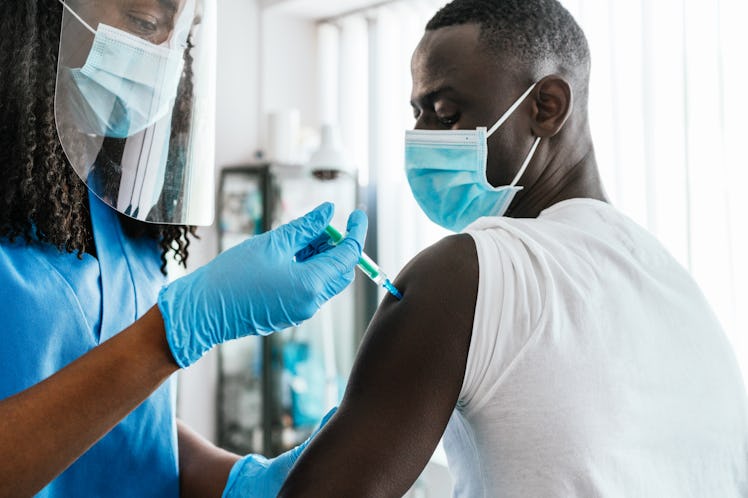 A healthcare provider in a mask and face shield gives a man in a mask the COVID booster.
