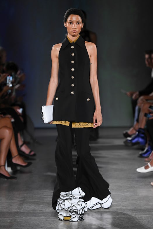 Lineisy Montero wears gold-buttoned long waistcoat and bell-bottom trousers with large contrasting r...