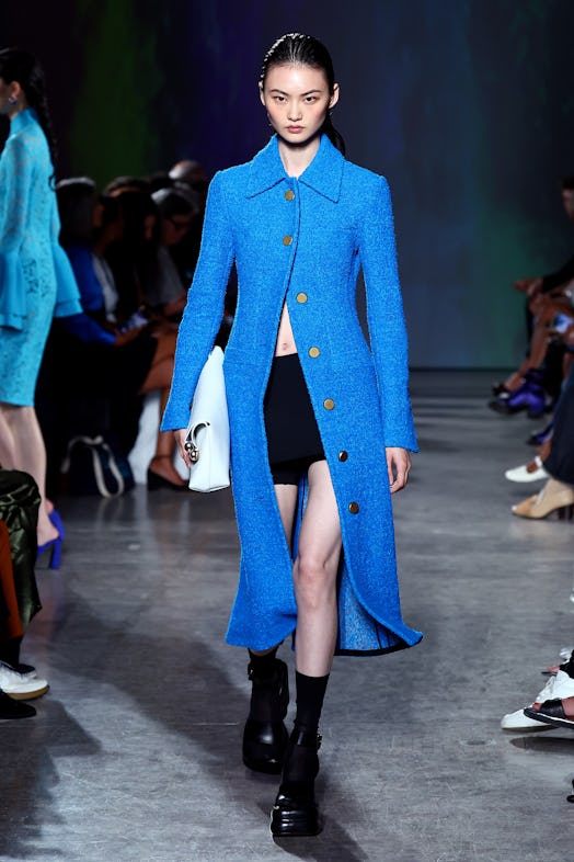 A model wears a bright blue, long, tailored coat with gold buttons by Proenza Schouler, paired with ...