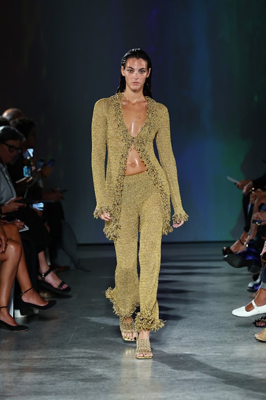 A model wears a see-through, fern-colored knit suit paired with matching slip-on heeled sandals. 