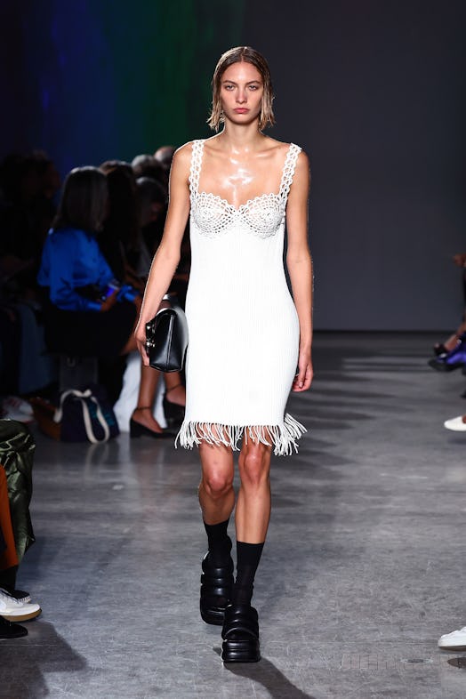 A model wears a corsetry-inspired white dress with fringing and chunky black platforms on the Proenz...