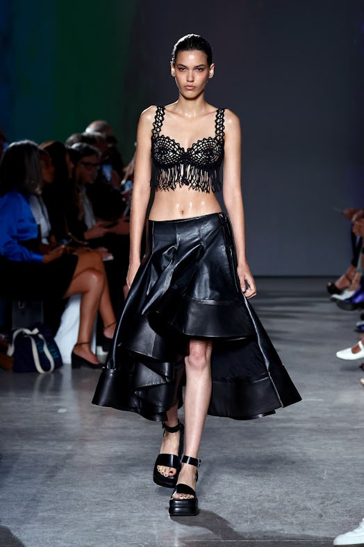 A model wears a loosely knit, fringed bustier matched with a cascading leather skirt and chunky plat...
