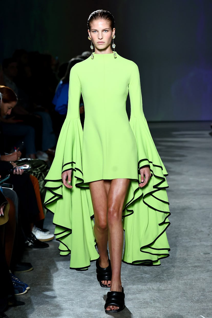 A model on the runway wears a Proenza Schouler short, high-neck lime green dress with layered bell s...