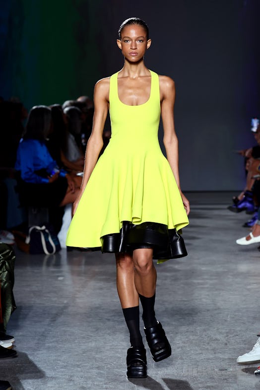 A model walks the runway in a full, bright yellow dress revealing a contrasting layer of black leath...
