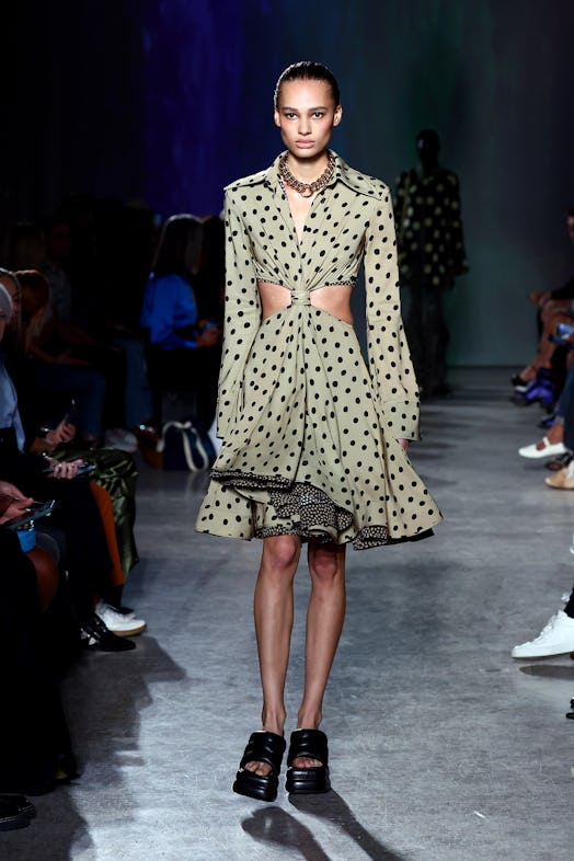 A model wears a full, polka-dot shirt dress featuring cut-outs, a front knot, and bell sleeves. 
