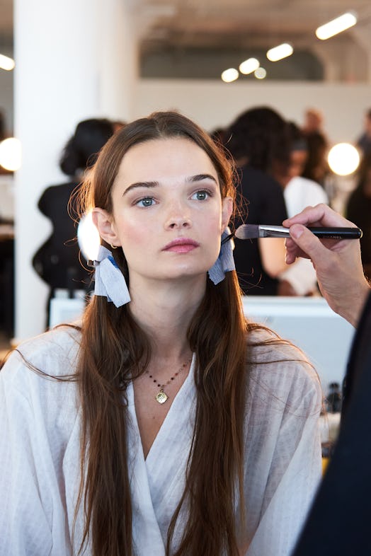 Woman with brown hair and pigtails getting her makeup done. 