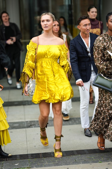 A guest wears a yellow gold shiny shoulder-off / long puffy sleeves / puffy short dress, a silver va...
