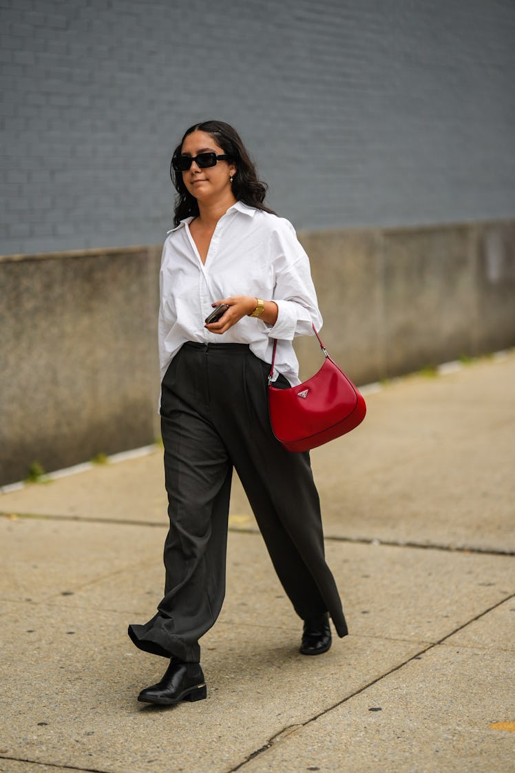 A guest wearing a white oversized shirt, black large pants, a red shiny Cleo Prada bag and a black s...