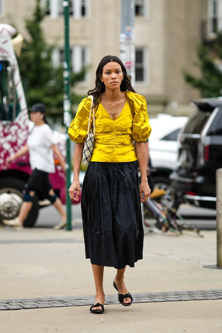 A guest wearing a gold long chain necklace, a bright yellow t-shirt, a white latter bag and a black ...