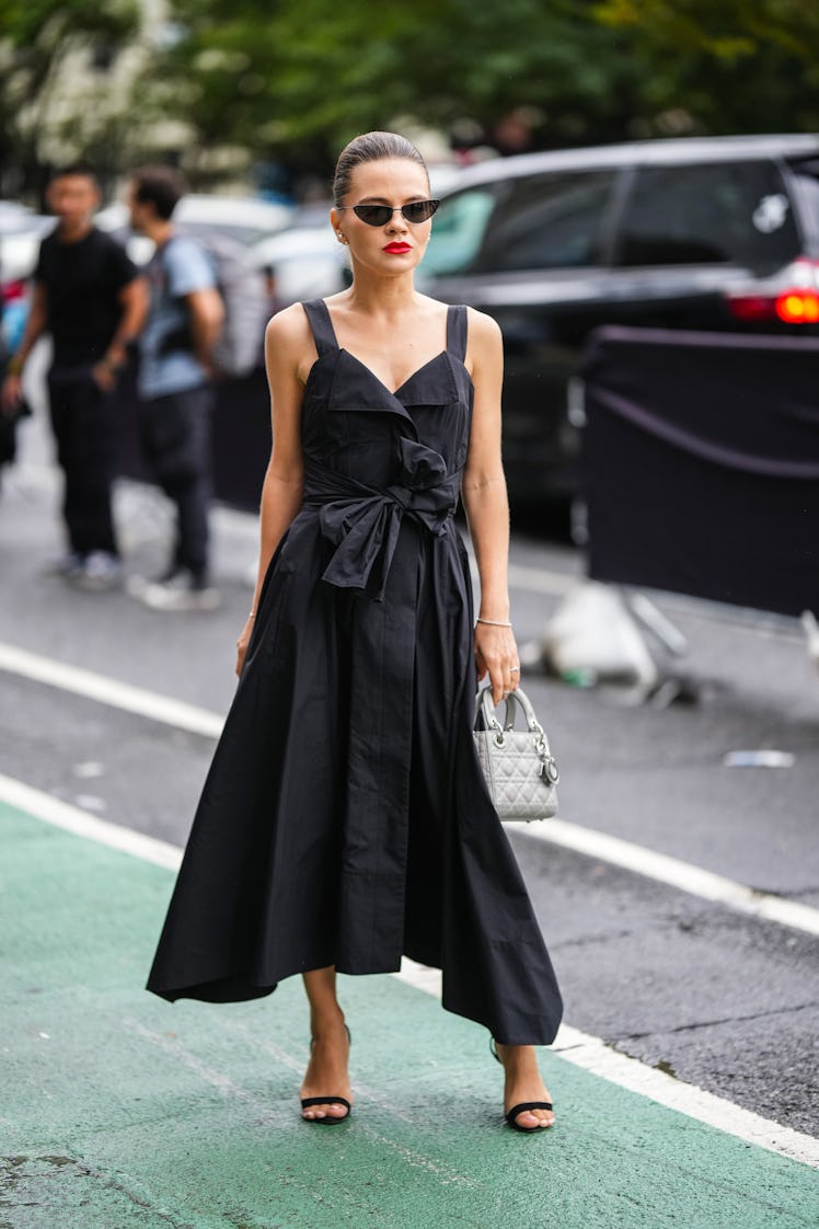 A guest wearing black heart-neck midi dress, a pale gray Lady D-Lite bag from Dior and black suede h...