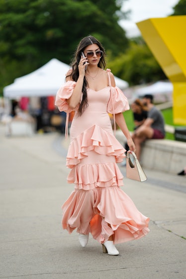 A guest wears brown sunglasses, a pale pink ruffled / shoulder-off / long dress, a white latte shiny...