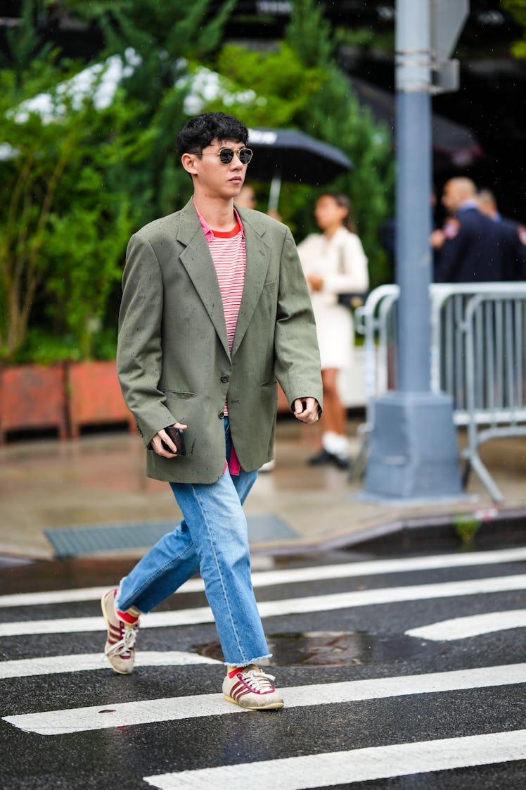 A guest wearing a red and beige striped t-shirt, a red long shirt, a khaki blazer jacket and blue de...
