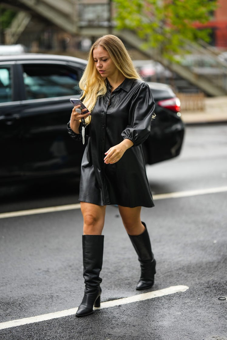 A guest wearing a black shiny leather shirt dress and black shiny high leather boots with block heel...