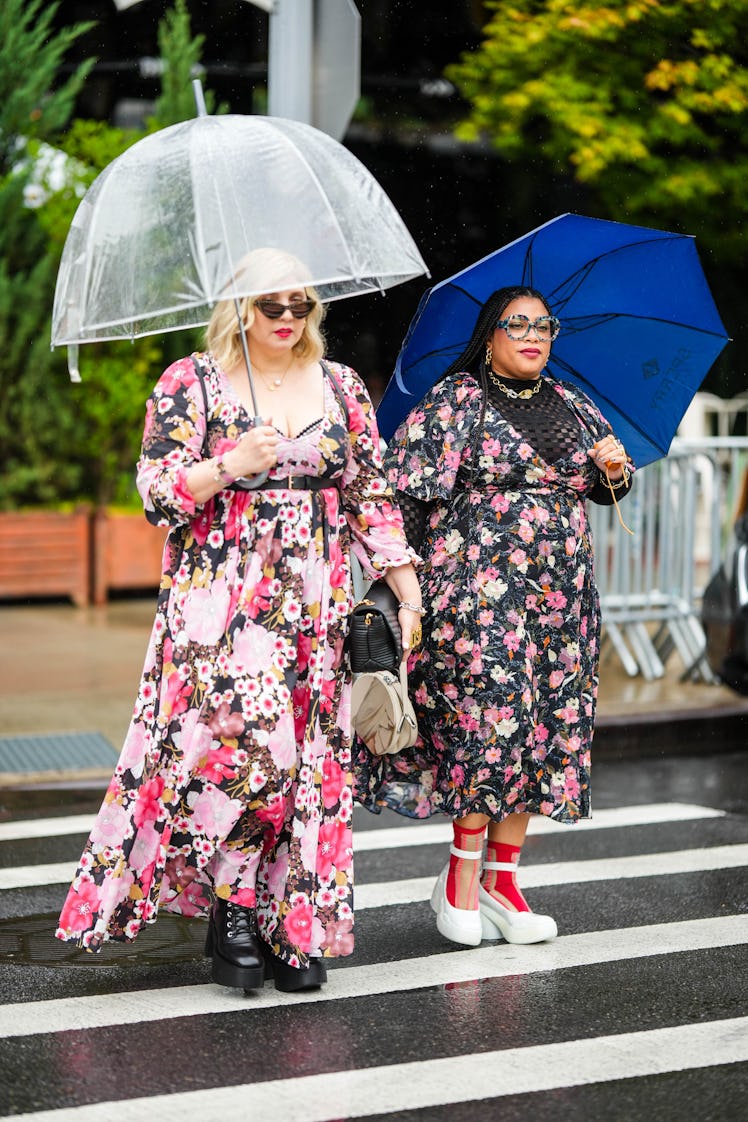 Two guests both wearing similar floral dresses and a transparent and a blue umbrella.
