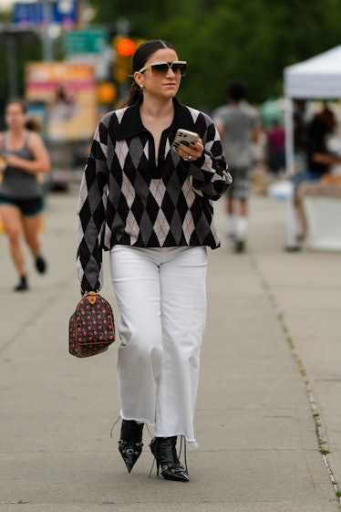  A guest wears beige and brown futurist sunglasses, silver rings, a black / gray / white checkered j...