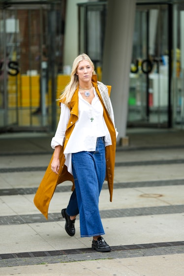 A guest wears diamond earrings, gold chain pendant necklaces, a yellow sleeveless mustard long gilet...